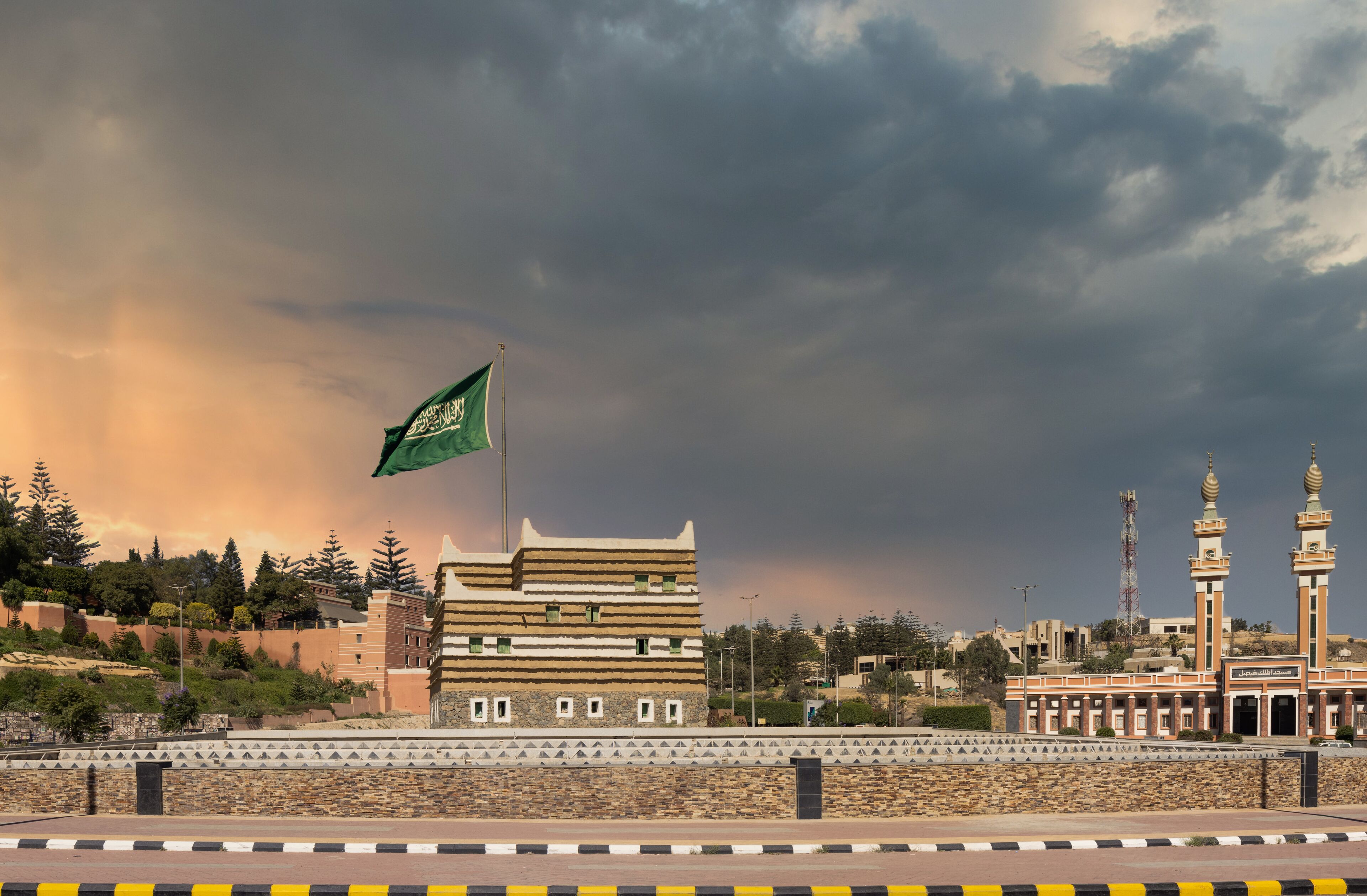 A building with a flag, a mosque with minarets, and a cloudy sky.