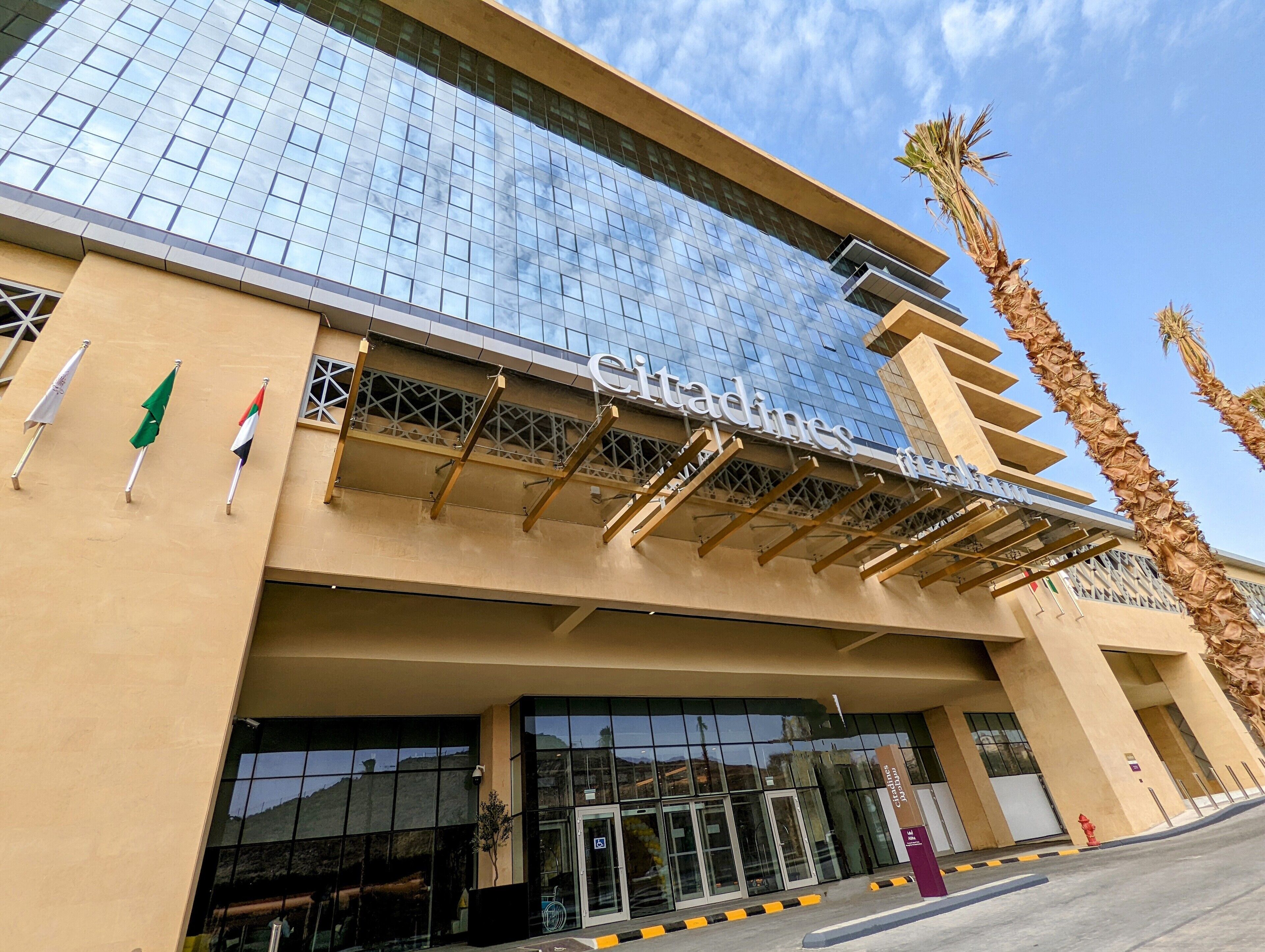 A hotel entrance with a glass facade, a name sign, and flags.