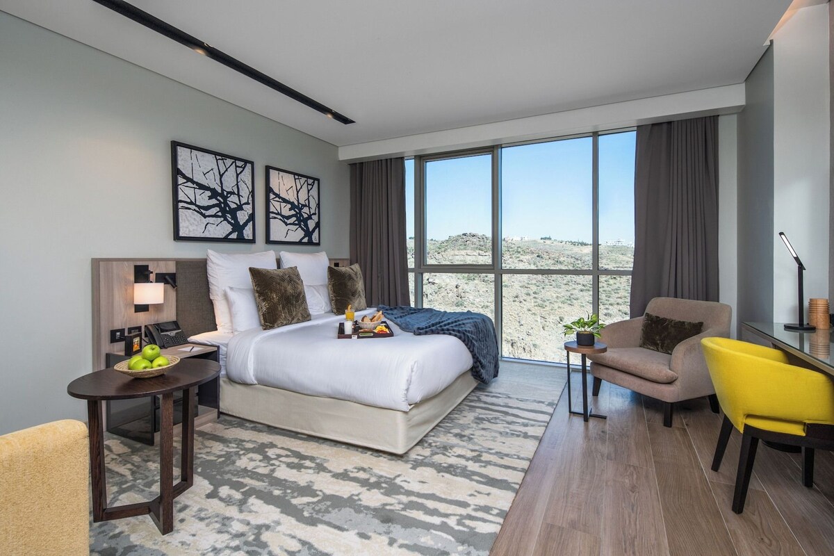 Habitación de hotel moderna con una cama grande, un escritorio, una silla y vistas al desierto.