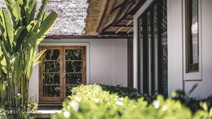 A house with a wooden door, a thatched roof, and a white exterior. - Kharista Villas & Retreat by Ekosistem (Canggu)