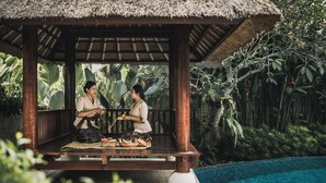 A wooden gazebo with a thatched roof overlooking a pool, surrounded by lush tropical vegetation. - Kharista Villas & Retreat by Ekosistem (Canggu)