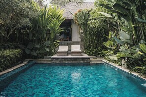 A pool with clear blue water, surrounded by lush tropical plants and a thatched-roof structure. - Kharista Villas & Retreat by Ekosistem (Canggu)