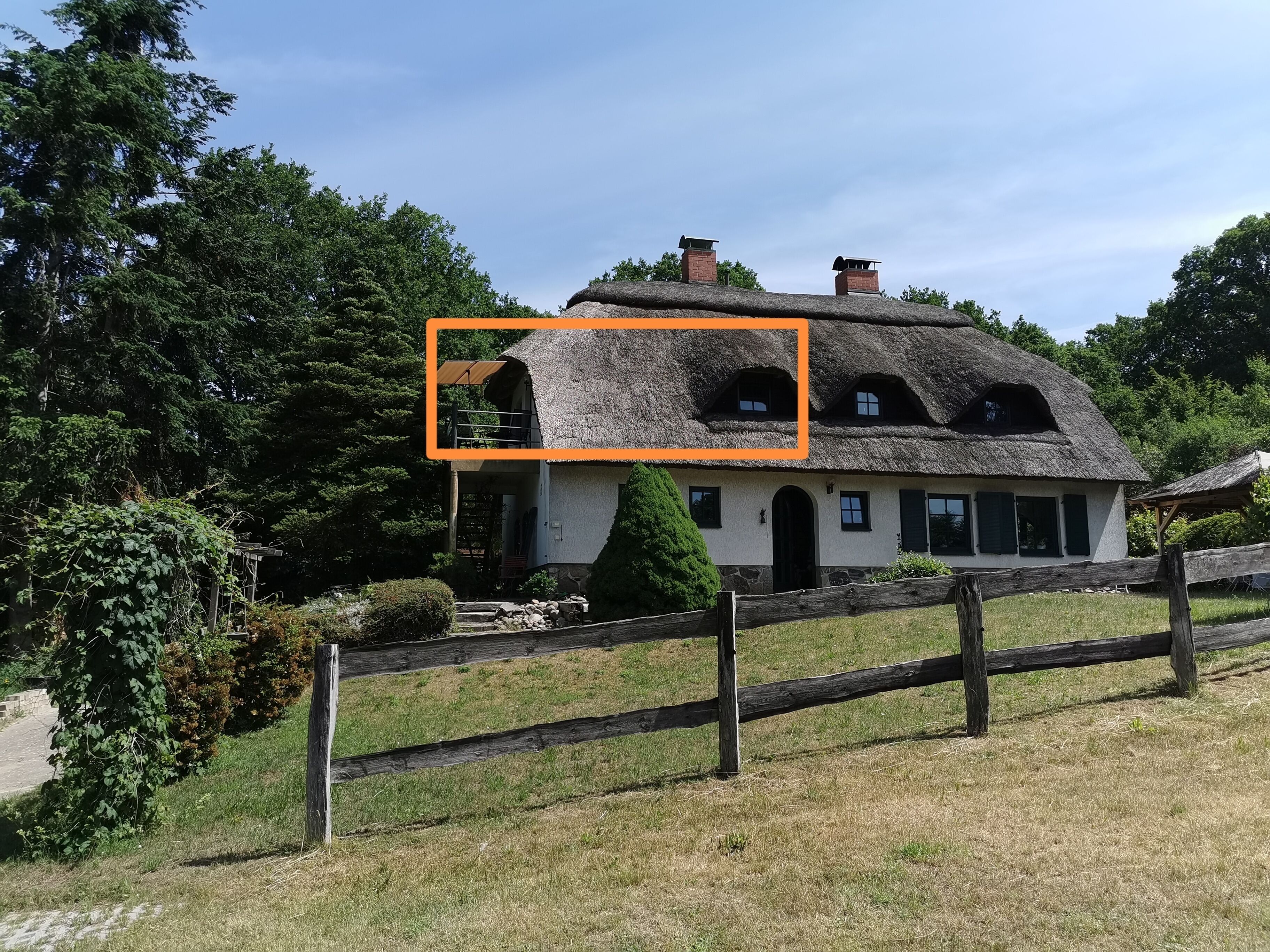 Une maison traditionnelle à toit de chaume, avec des fondations en pierre, une clôture en bois et un jardin bien entretenu.