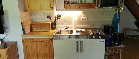 Una cocina compacta con armarios de madera, estufa, pileta y microondas.