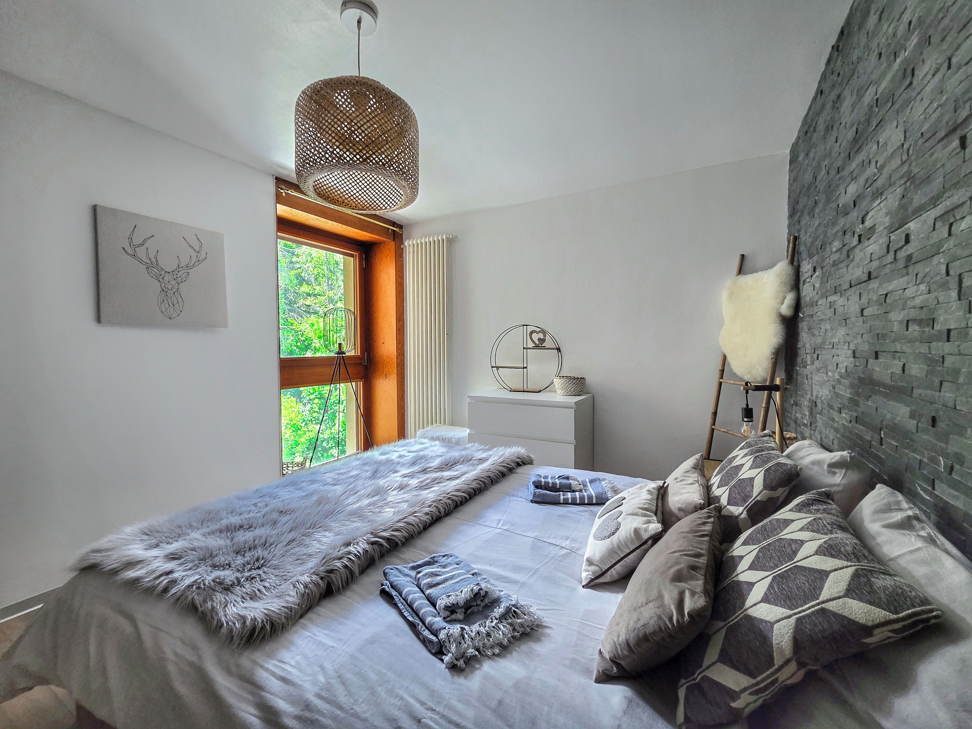 Een slaapkamer met een bed, een raam, een wandplank en een hanglamp.