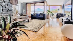 Un salón moderno con pared de piedra, suelo de madera y ventanas amplias que ofrecen vistas a la montaña.