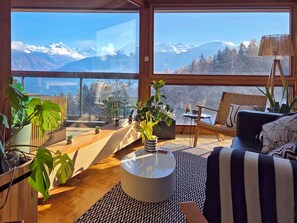 Un salon spacieux doté d’une grande fenêtre offrant une vue sur les montagnes, d’un parquet en bois, d’une table basse ronde et d’un canapé à rayures.