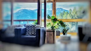 Una sala de estar moderna con un sofá, una planta en maceta y grandes ventanales con vistas a la montaña.