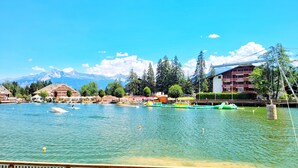 Vista al lago con barcos, una terraza de madera y edificios al fondo.