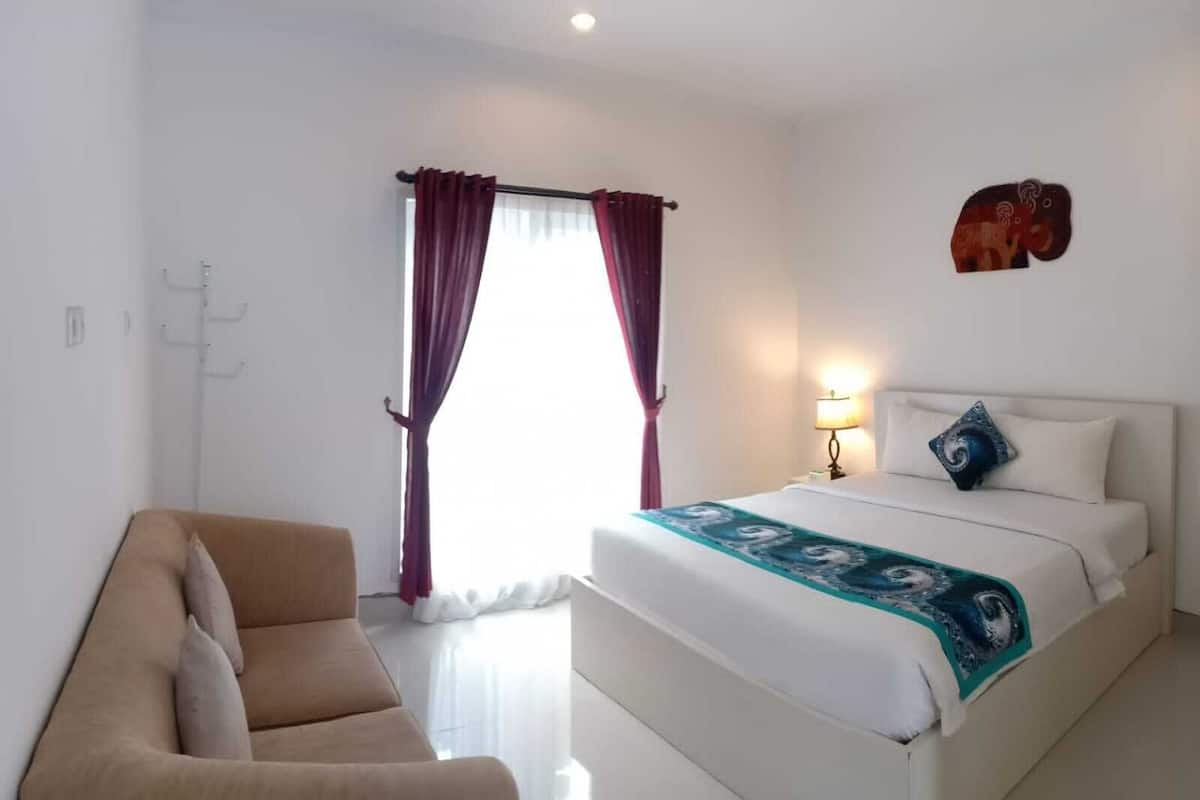 A hotel room with a bed, a chair, a lamp, and a window with curtains.