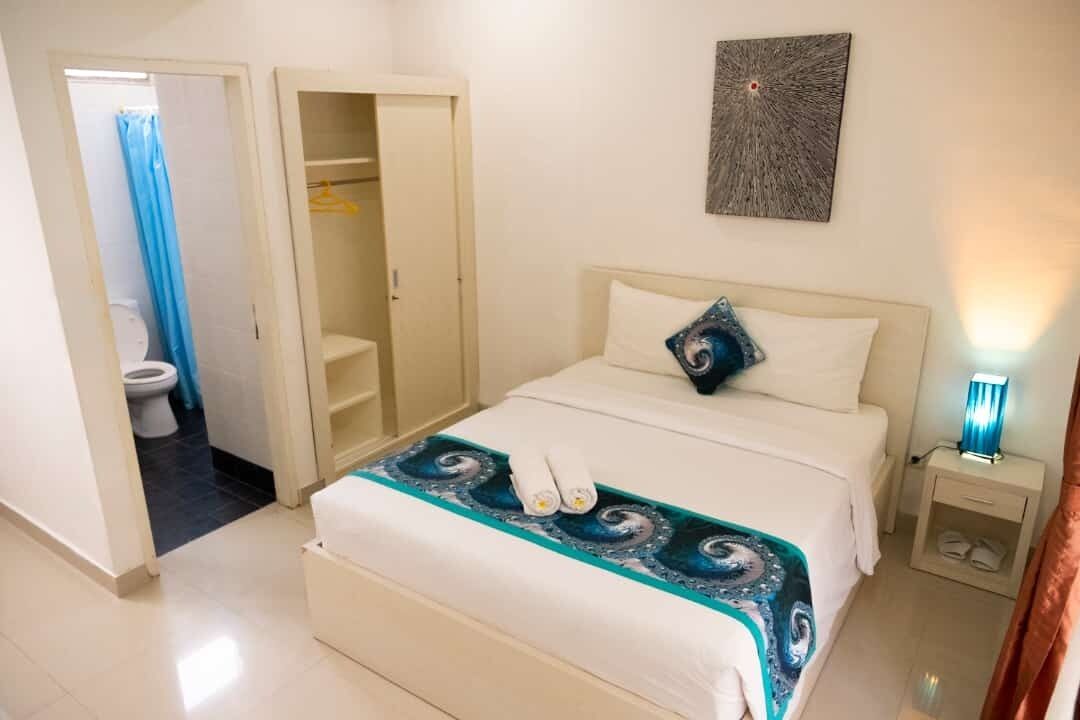 A hotel room with a bed, a nightstand, a wall-mounted artwork, and a bathroom visible through an open door.