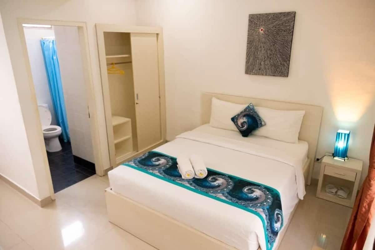 A hotel room with a bed, a nightstand, a wall-mounted artwork, and a bathroom visible through an open door.