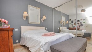 Een slaapkamer met een bed, een bankje, een dressoir en een spiegel.