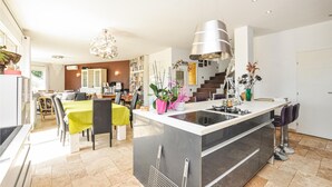 Een moderne keuken met een centraal eiland, een eethoek met stoelen en een tafel, en een trap die naar een ander niveau leidt.