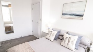Quarto com cama, almofadas, mesa de cabeceira, luminária, espelho e pintura na parede.