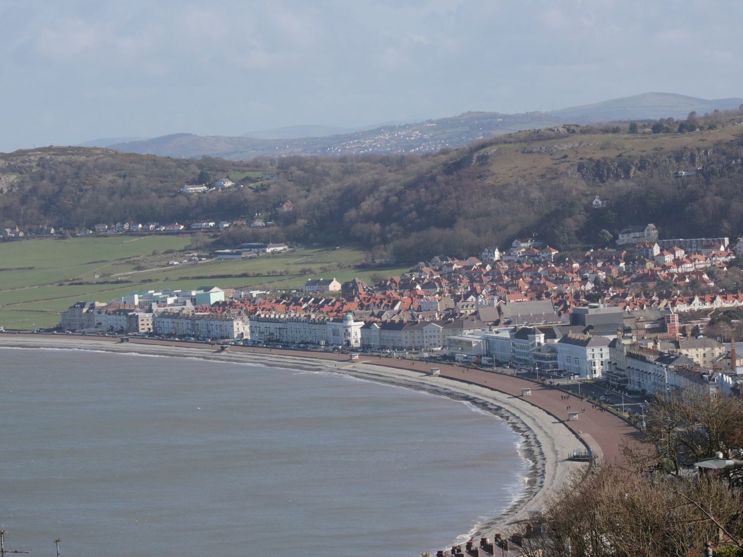 Une ville côtière avec une plage, des bâtiments et des collines en arrière-plan.
