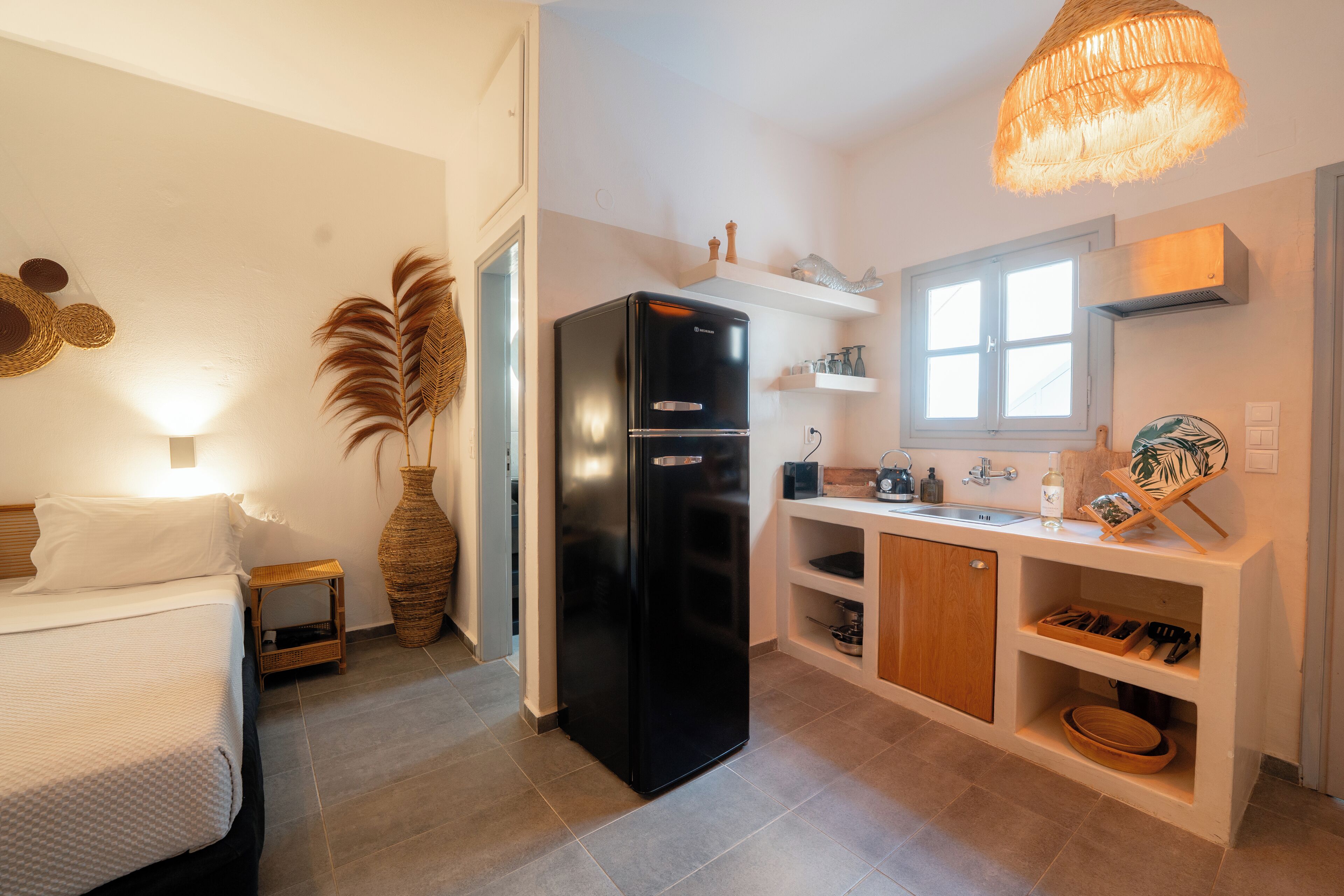 A compact kitchen with a black refrigerator, a wooden cabinet, and a window above the sink.