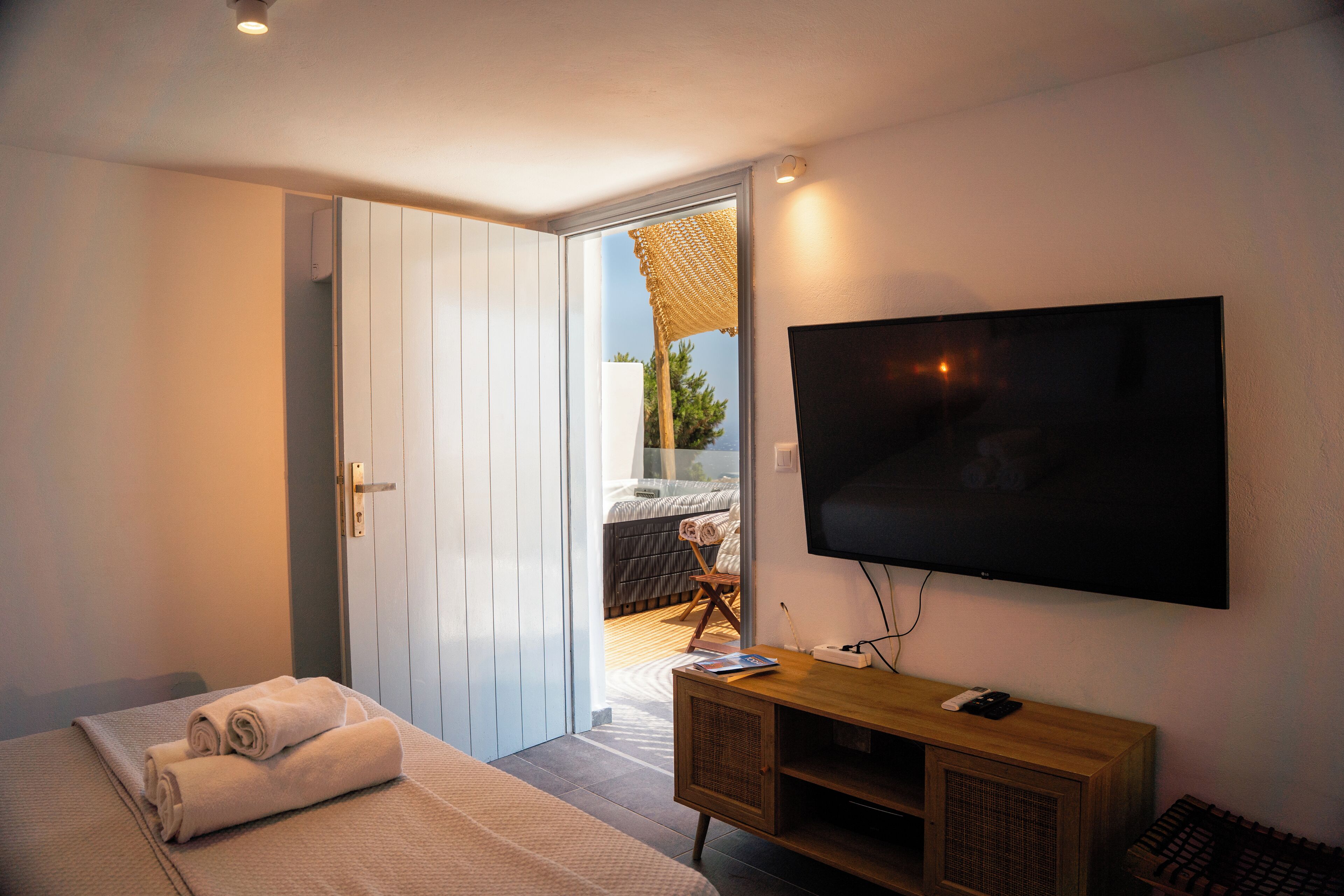 A bedroom with a bed, a TV mounted on the wall, a wooden console table, and a door leading to a balcony.