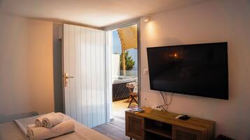 Een slaapkamer met een bed, een aan de muur bevestigde televisie, een houten console en een deur naar een balkon.