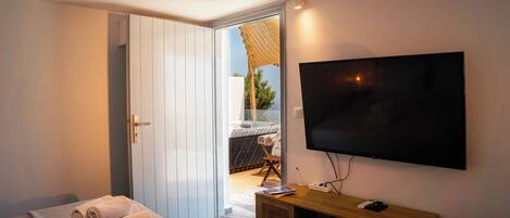 A bedroom with a bed, a TV mounted on the wall, a wooden console table, and a door leading to a balcony.