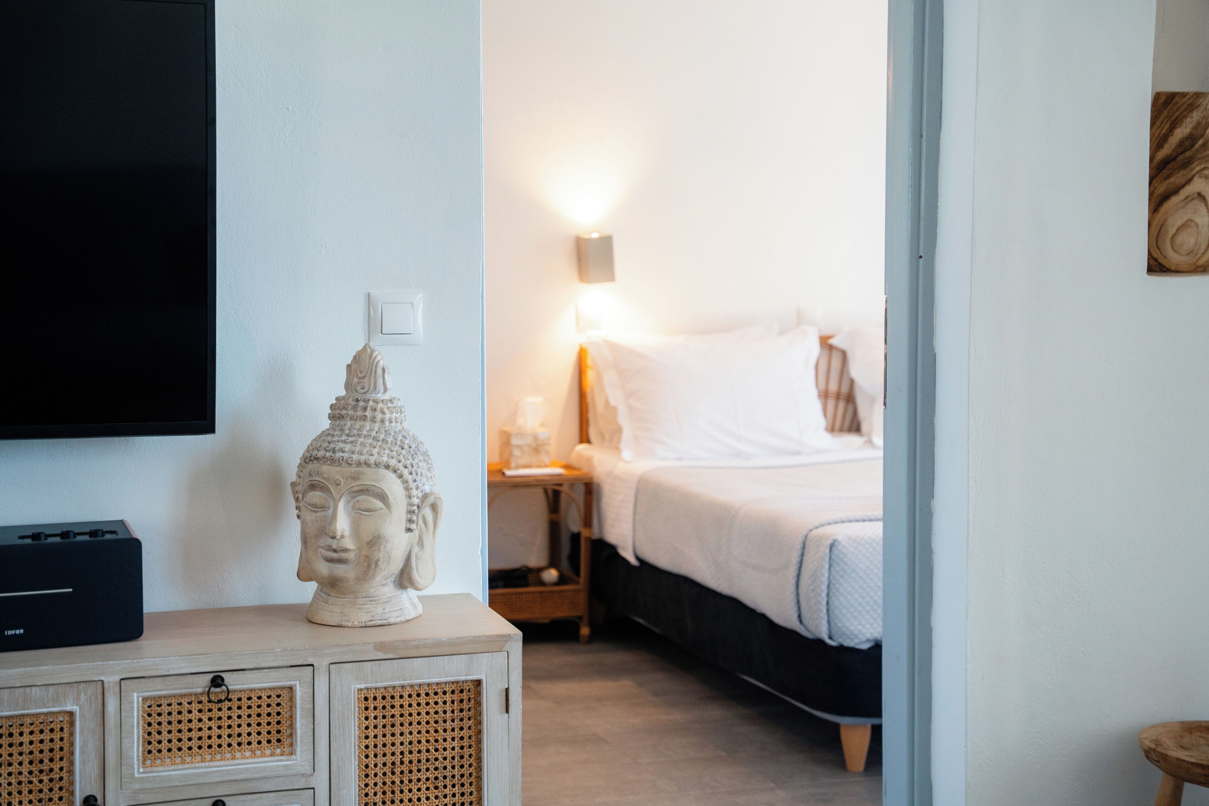 Un dormitorio con cama, mesita de noche, lámpara y una estatua de Buda sobre un mueble.