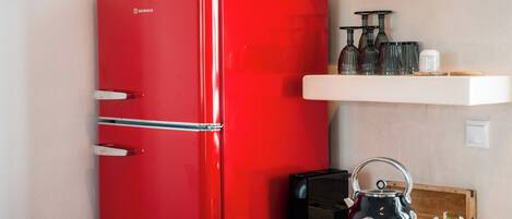 A red refrigerator, a black kettle, and a shelf with glasses and a salt shaker.
