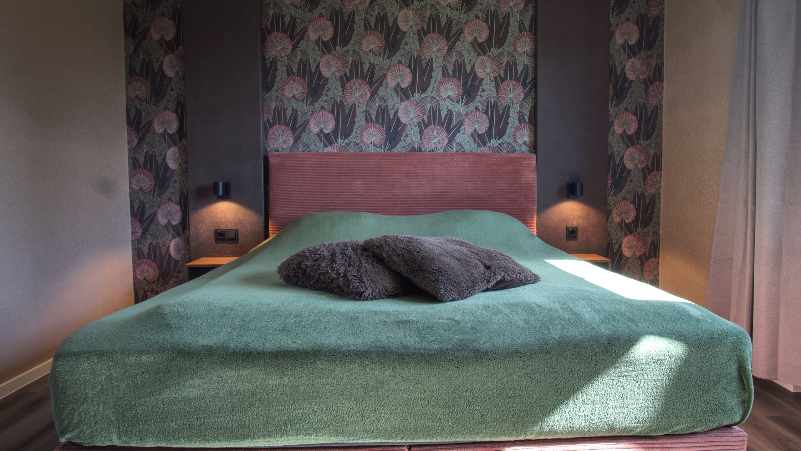 Una cama con cubierta verde, dos almohadas y dos lámparas fijadas a la pared.