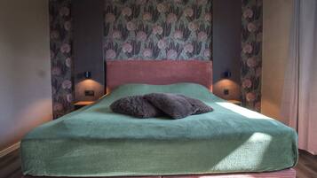 Una cama con cubierta verde, dos almohadas y dos lámparas fijadas a la pared.