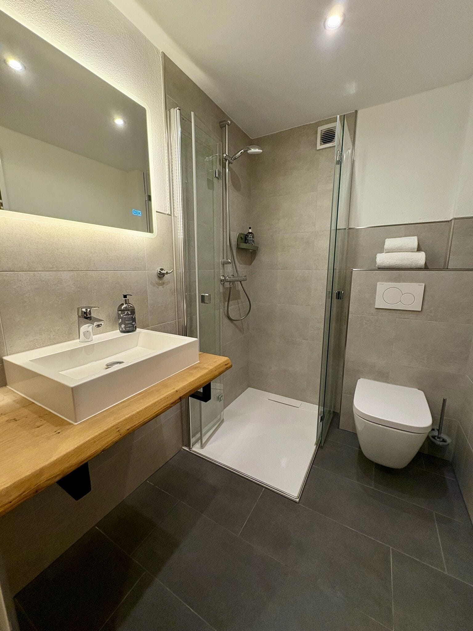 A modern bathroom with a glass-enclosed shower, a white sink with a wooden countertop, and a toilet.