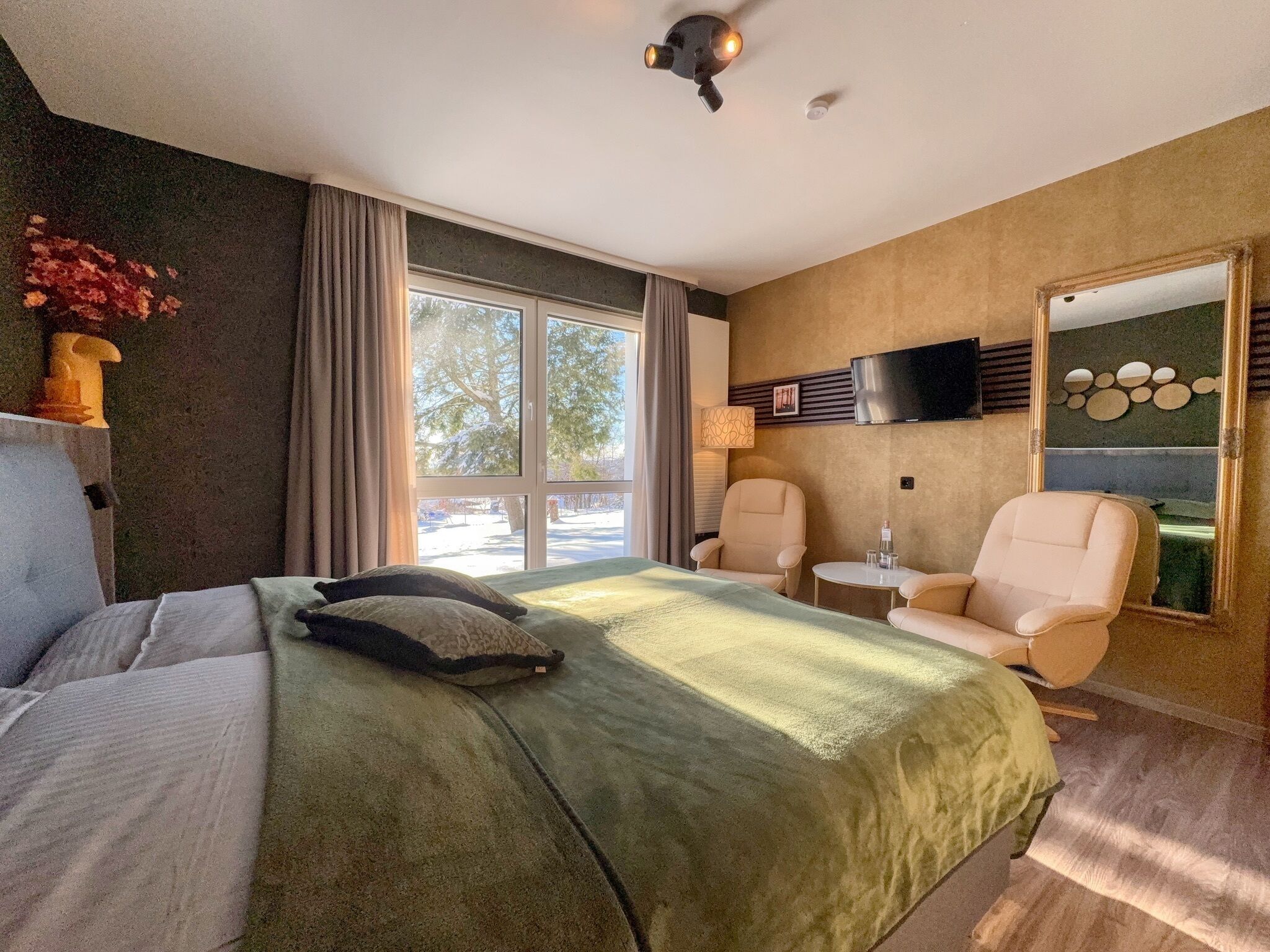 Een hotelkamer met een groot bed, twee fauteuils, een tafeltje, een televisie en een raam met gordijnen.