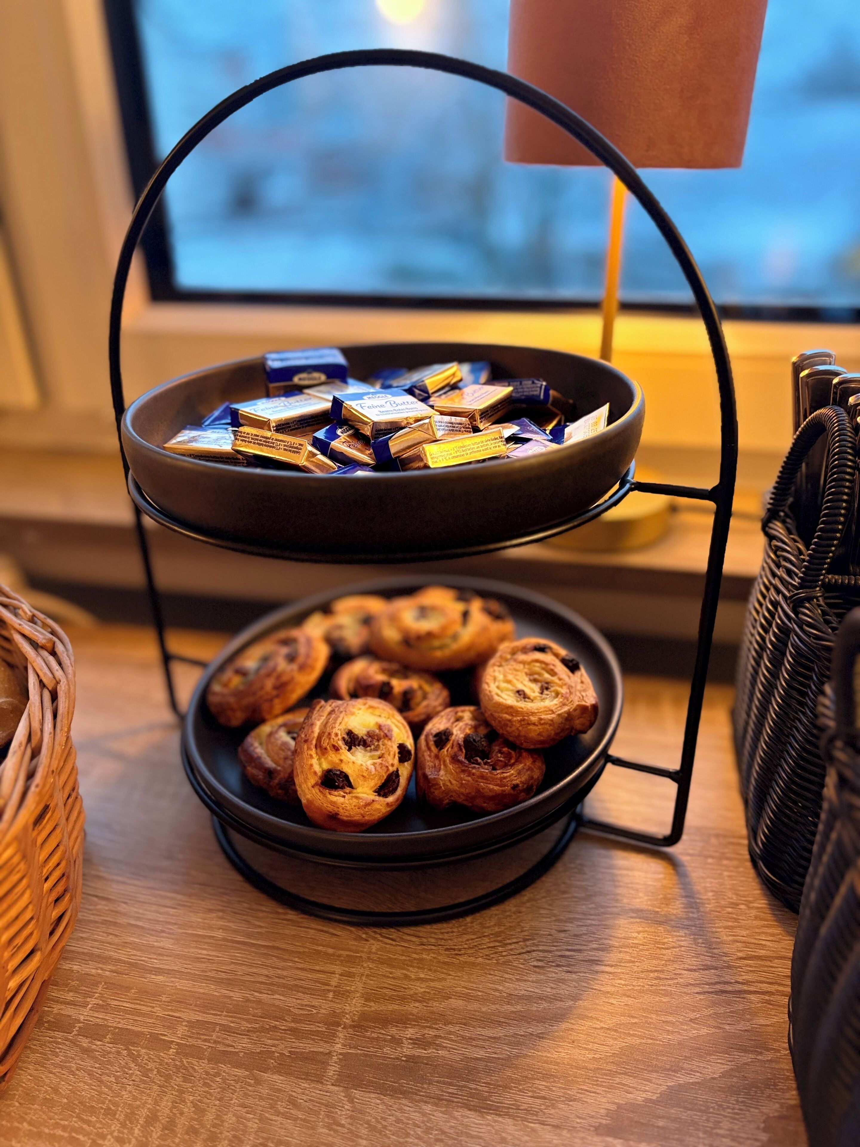 A two-tiered tray stand holding chocolates and pastries on a wooden table.