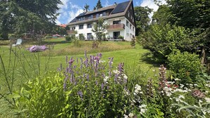 A two-story house with a sloped roof and solar panels, surrounded by lush greenery and flowering plants. - Berghotel Hohegeiß (Braunlage)