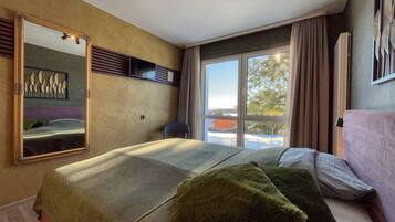 A bedroom with a bed, a large mirror, a window with curtains, and a view of the outside.