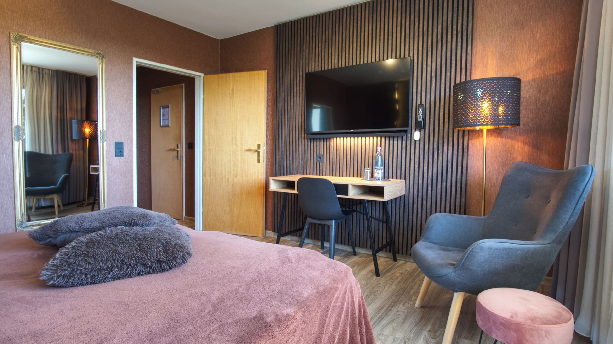 A hotel room with a bed, a desk, a chair, a television, and a lamp.