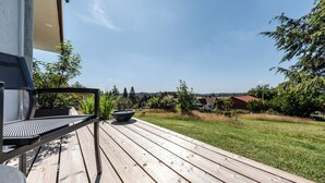 A wooden deck with a grill and seating area, overlooking a grassy yard and houses in the distance. - Berghotel Hohegeiß (Braunlage)