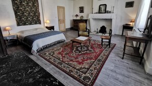Een traditionele kamer met een bed, een houten stoel, een tafel en een open haard.