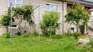 Una casa amb jardí, incloent una pergola, un arbre petit i un arbre més gran amb flors vermelles.