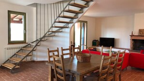 A dining area with a wooden table and chairs, a staircase with wooden steps, a television, and a fireplace. - Charming 3 Bed Villa in Otricoli Stunnings Views (Otricoli)