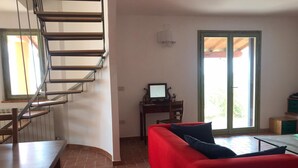 A modern living room with a red sofa, a wooden dining table, a staircase, a desk with a computer, and a sliding glass door leading to an outdoor area. - Charming 3 Bed Villa in Otricoli Stunnings Views (Otricoli)