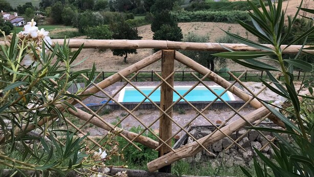 A pool surrounded by a bamboo fence with a view of rolling hills and a distant village. - Charming 3 Bed Villa in Otricoli Stunnings Views (Otricoli)