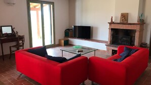 A living room with red sofas, a glass coffee table, a TV, a fireplace, and a desk with a computer. - Charming 3 Bed Villa in Otricoli Stunnings Views (Otricoli)