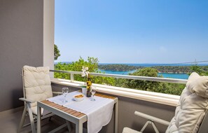 A balcony with a table set for two, overlooking a scenic coastal landscape.