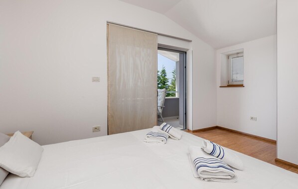 Ein Schlafzimmer mit Bett, zwei Kissen, einem Fenster und einer Tür, die auf einen Balkon führt.