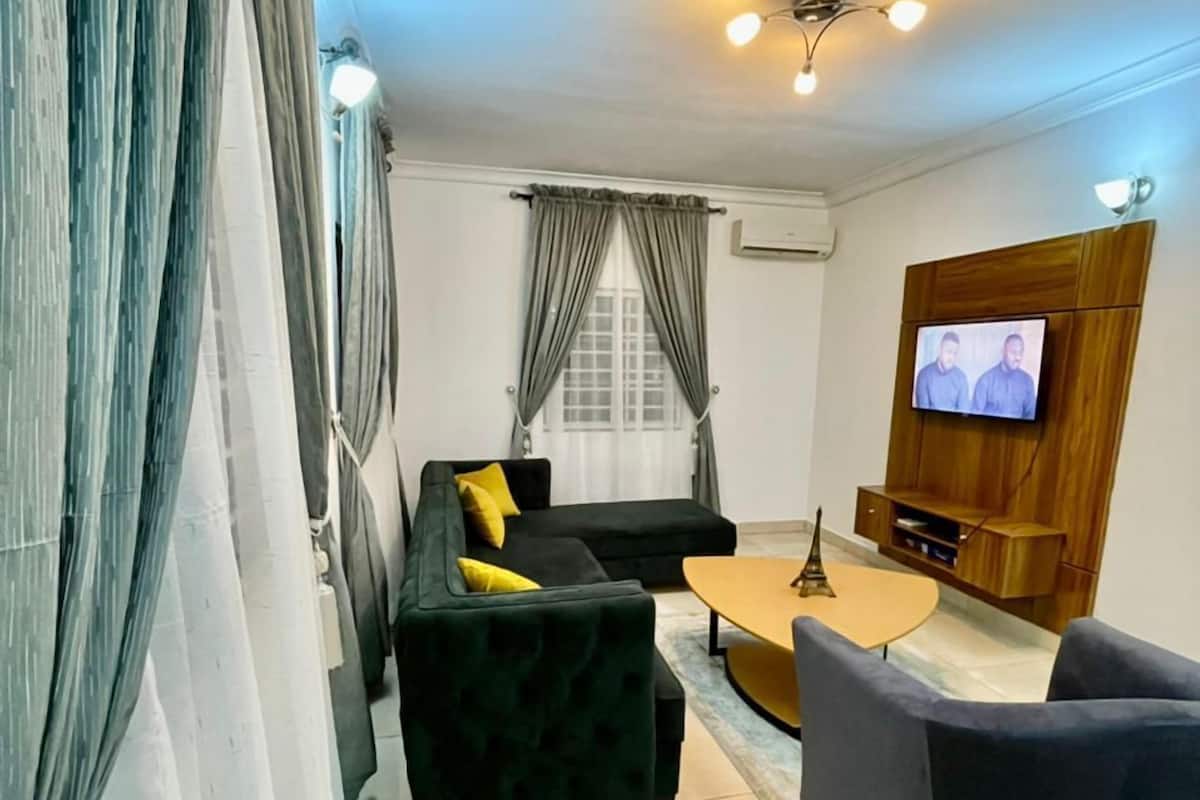 A modern living room with a sofa, armchairs, a coffee table, and a TV mounted on the wall.