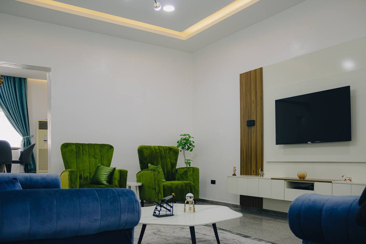 A modern living room with a flat-screen TV, green upholstered chairs, and a blue sofa.