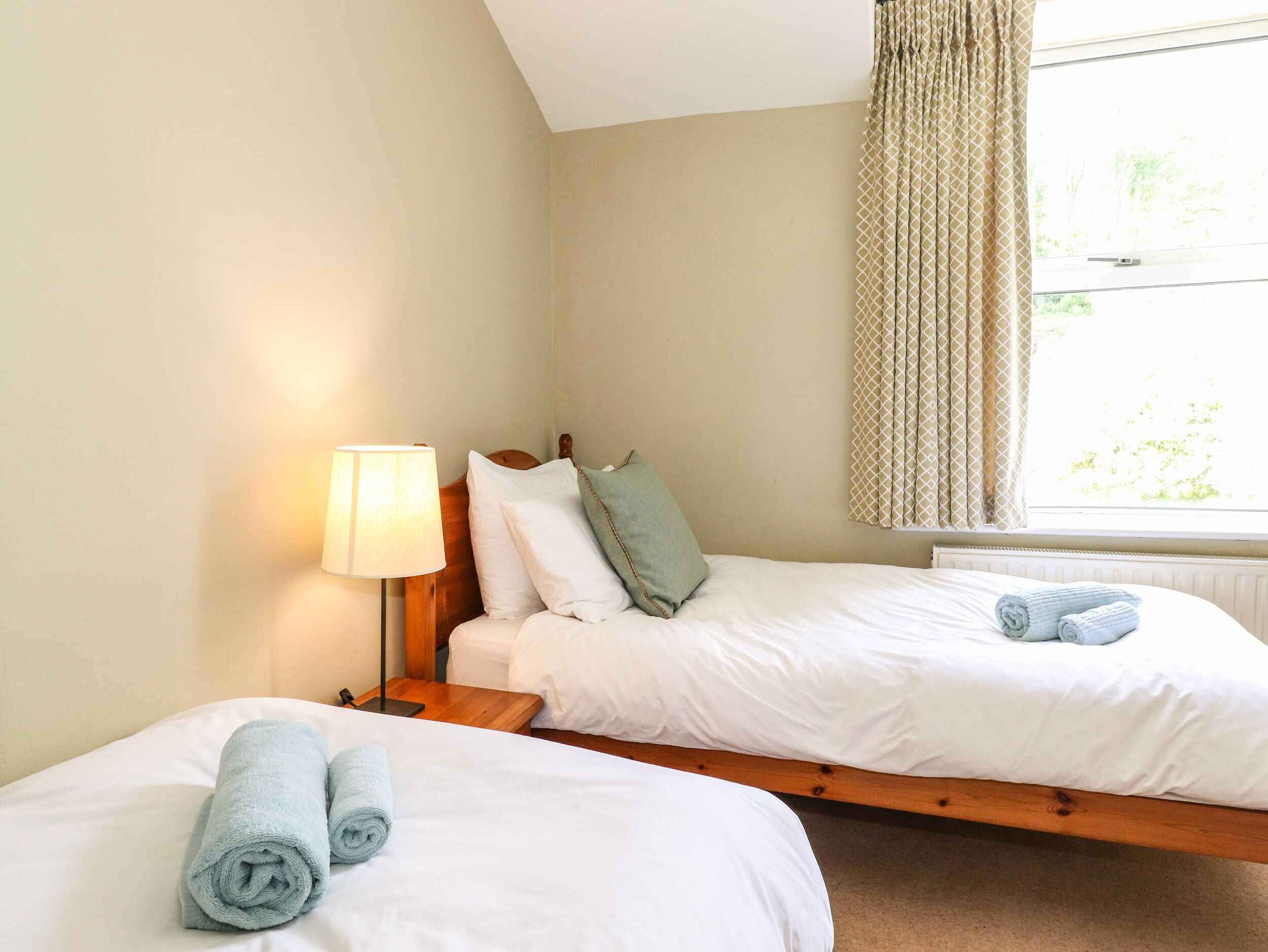 A hotel room with two single beds, a bedside lamp, and a window with curtains.