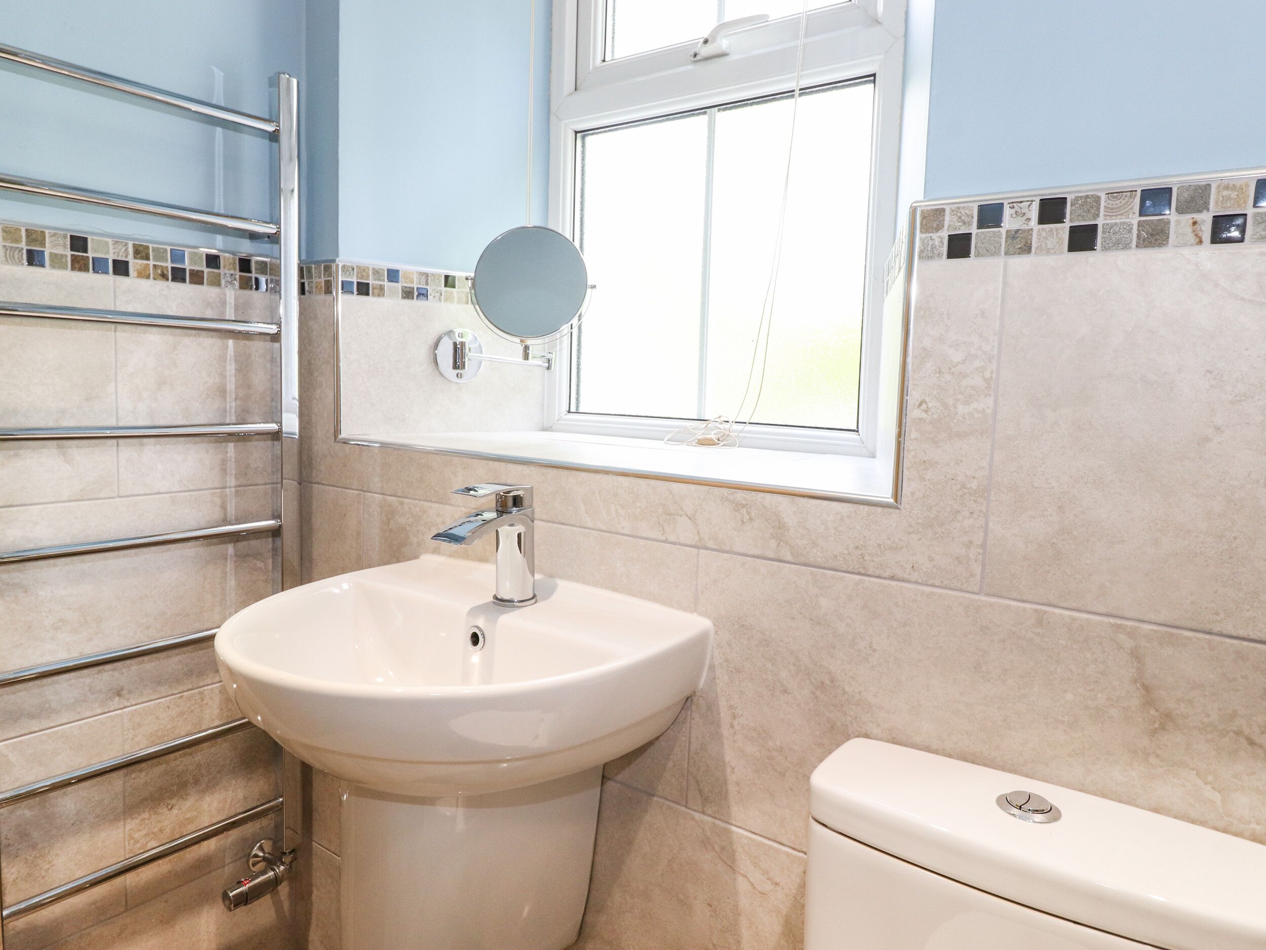 A bathroom with a white sink, a mirror, a window, and a toilet.