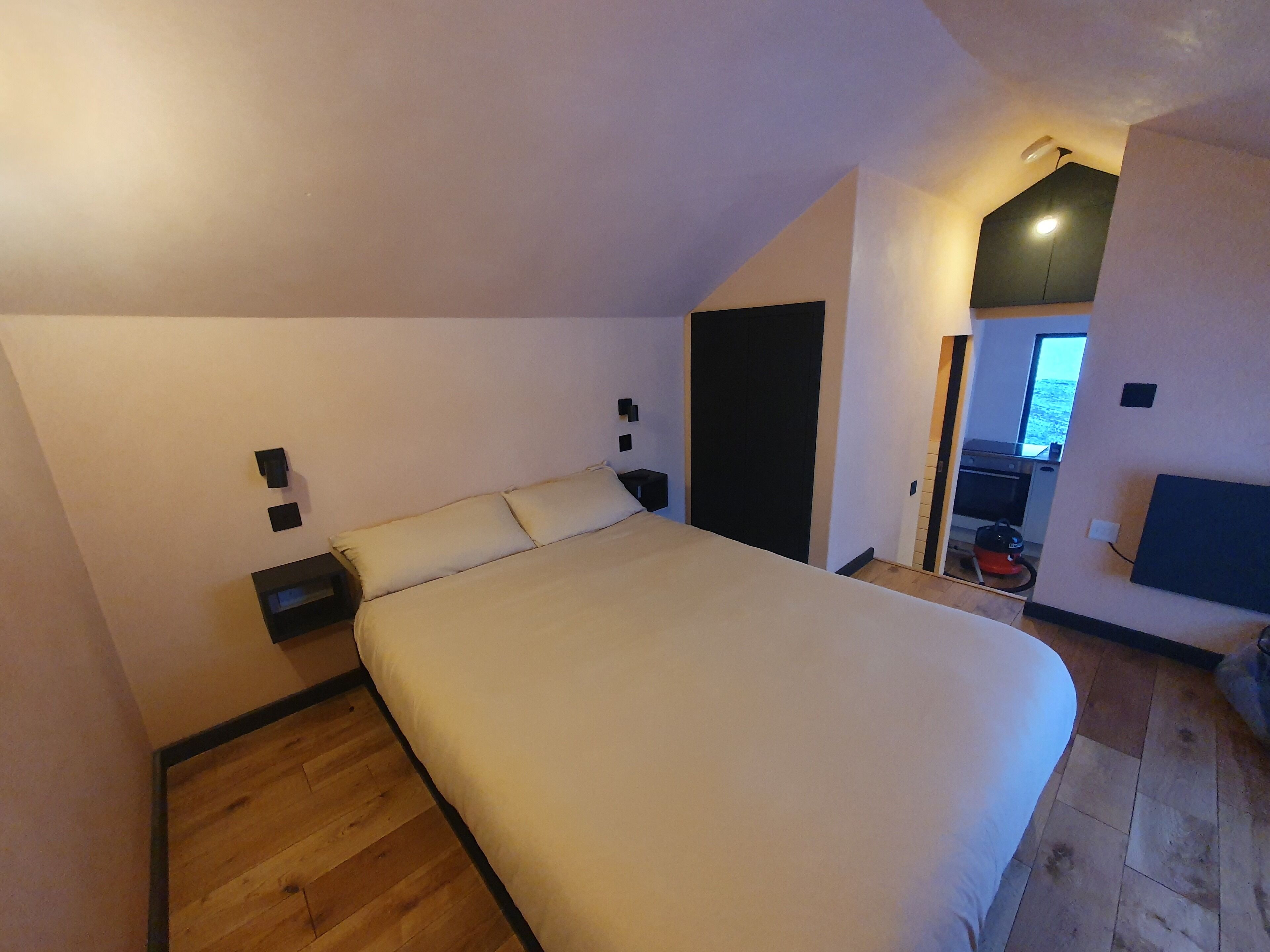 Ein Schlafzimmer mit einem großen Bett, Holzboden, einem schwarzen Kleiderschrank und einem kleinen Nachttisch.