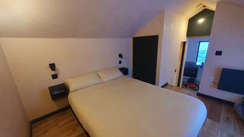 Ein Schlafzimmer mit einem großen Bett, Holzboden, einem schwarzen Kleiderschrank und einem kleinen Nachttisch.