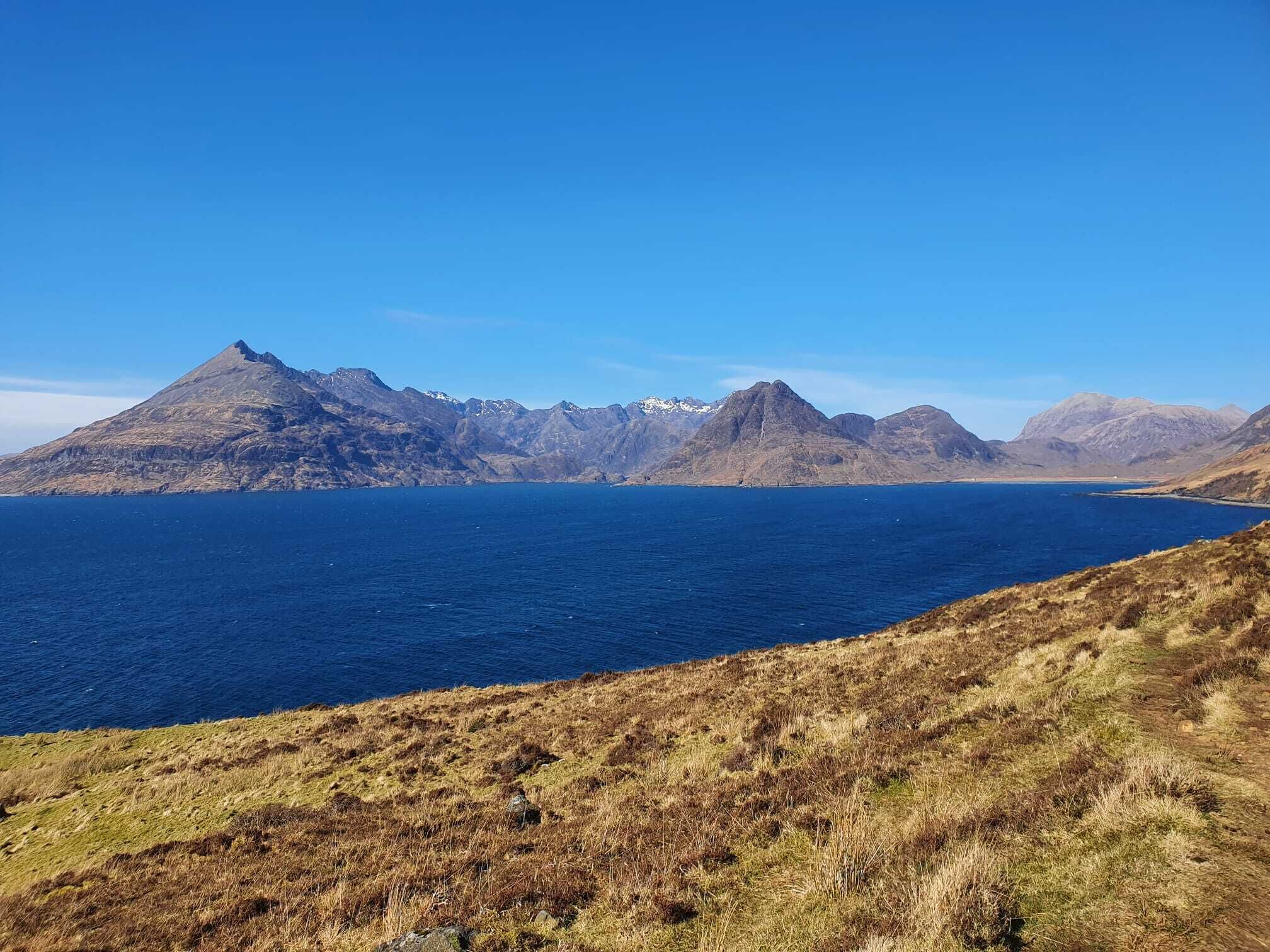 A coastal landscape with a prominent mountain range and a clear blue sea.